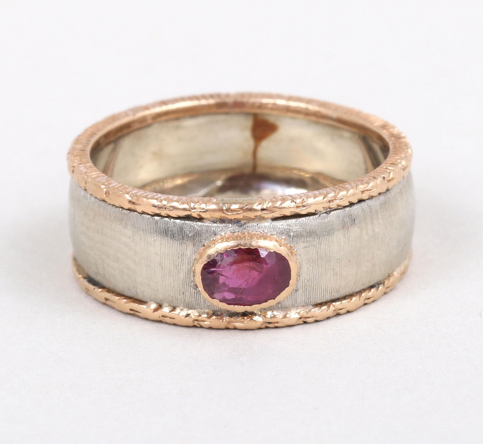 Buccellati 18k Ruby Ring: Buccellati 18k Ruby Ringhaving an oval-cut ruby in a rose gold bezel setting with incised geometric design, on a textured white gold band having applied rose gold borders with foliate design, signed i