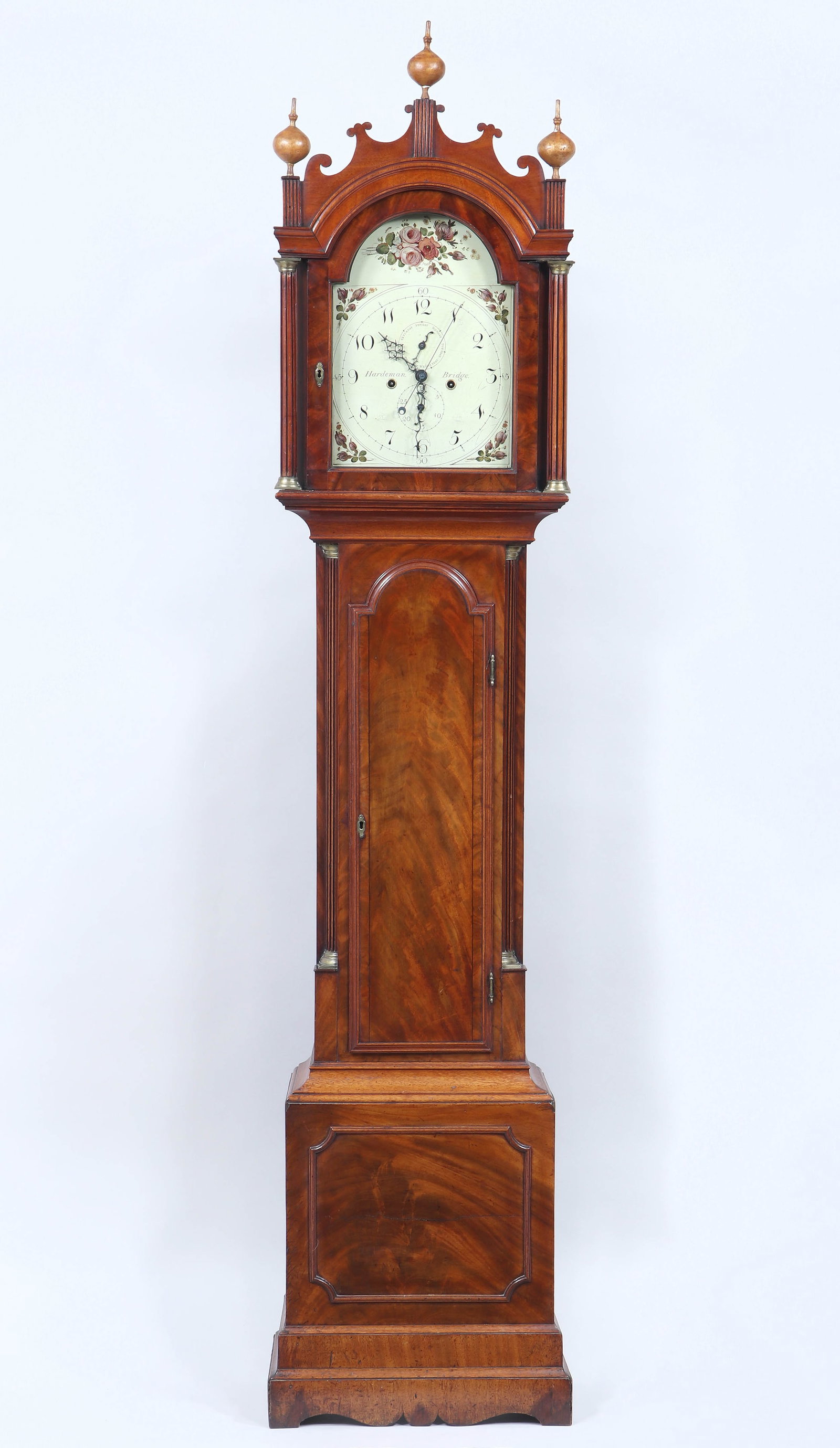 Samuel Hardeman Tall Case Clock: Samuel Hardeman Figured Mahogany Tall Case Clock Bridge, England, 18th/19th Century the arched bonnet surmounted by a shaped crest and three painted and carved ball-and-spire finials on fluted upright