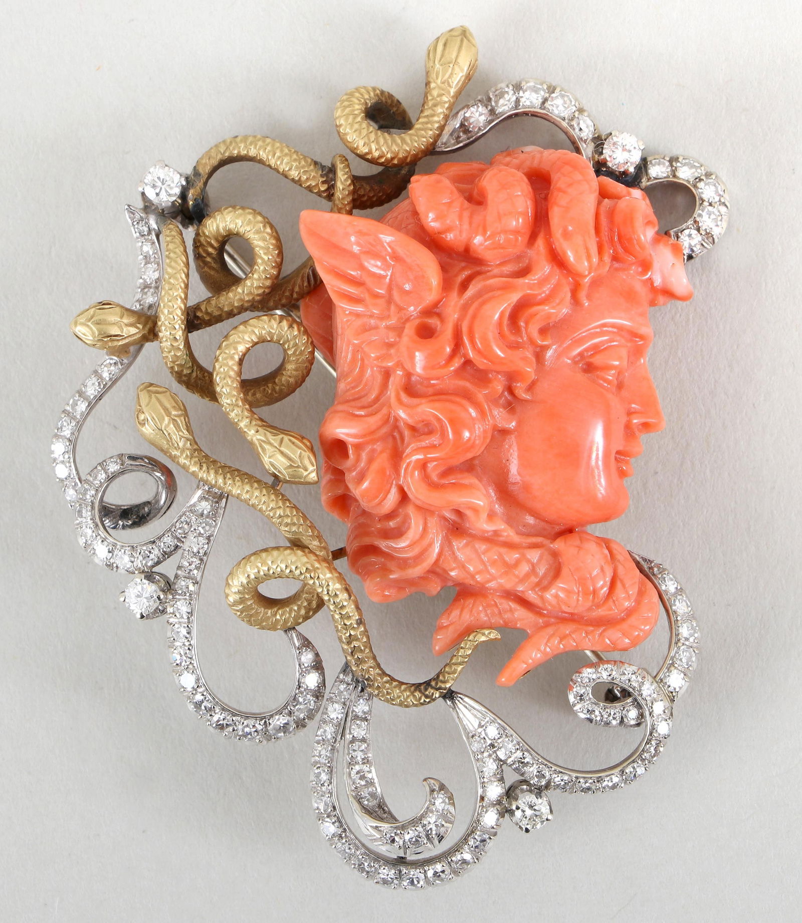 Coral Cameo, Diamond, and 18k Gold Medusa Brooch: Coral Cameo, Diamond, and 18k Gold Medusa Broochhaving a coral cameo depicting the winged head of Medusa, surrounded by yellow gold snakes and white gold scrolls with (102) round-cut diamonds of varyi