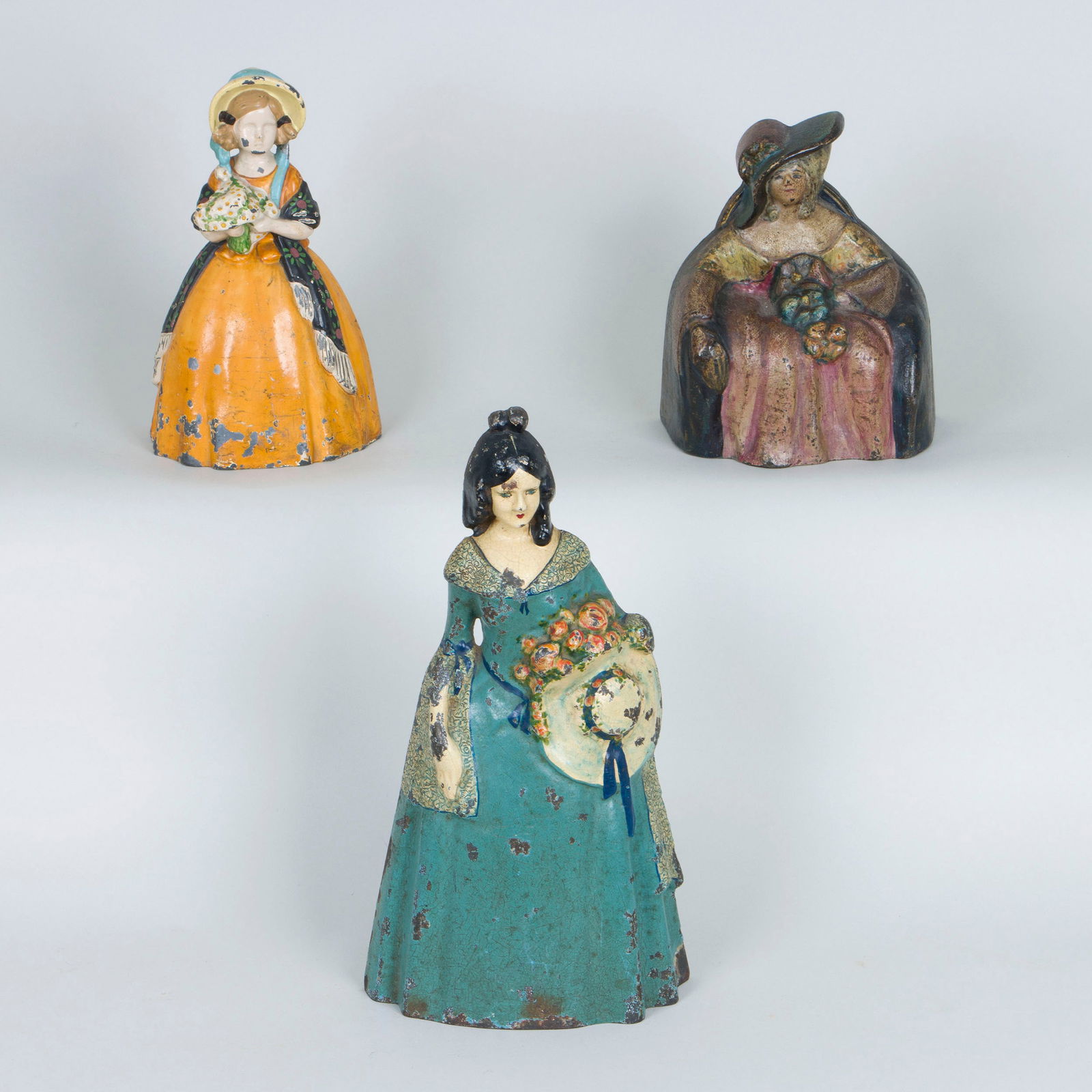 Colonial and Victorian Women Figural Doorstops: Group of (3) Colonial and Victorian Women Figural Doorstopsto include: painted pot metal doorstop in the form of a girl with a bonnet and a bouquet of flowers; and (2) painted cast iron doorstops, one