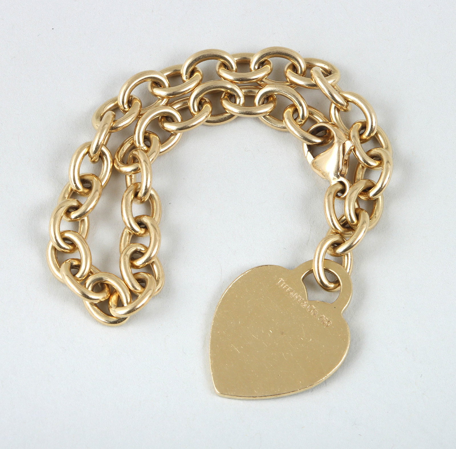 Tiffany & Co. 18k Gold "Heart Tag" Bracelet: Tiffany & Co. 18k Gold "Heart Tag" Bracelethaving a heart-form charm on a cable chain with oval links, marked on clasp and charm; along with Tiffany & Co. pouch having a snap closure.Length (open) 7 3
