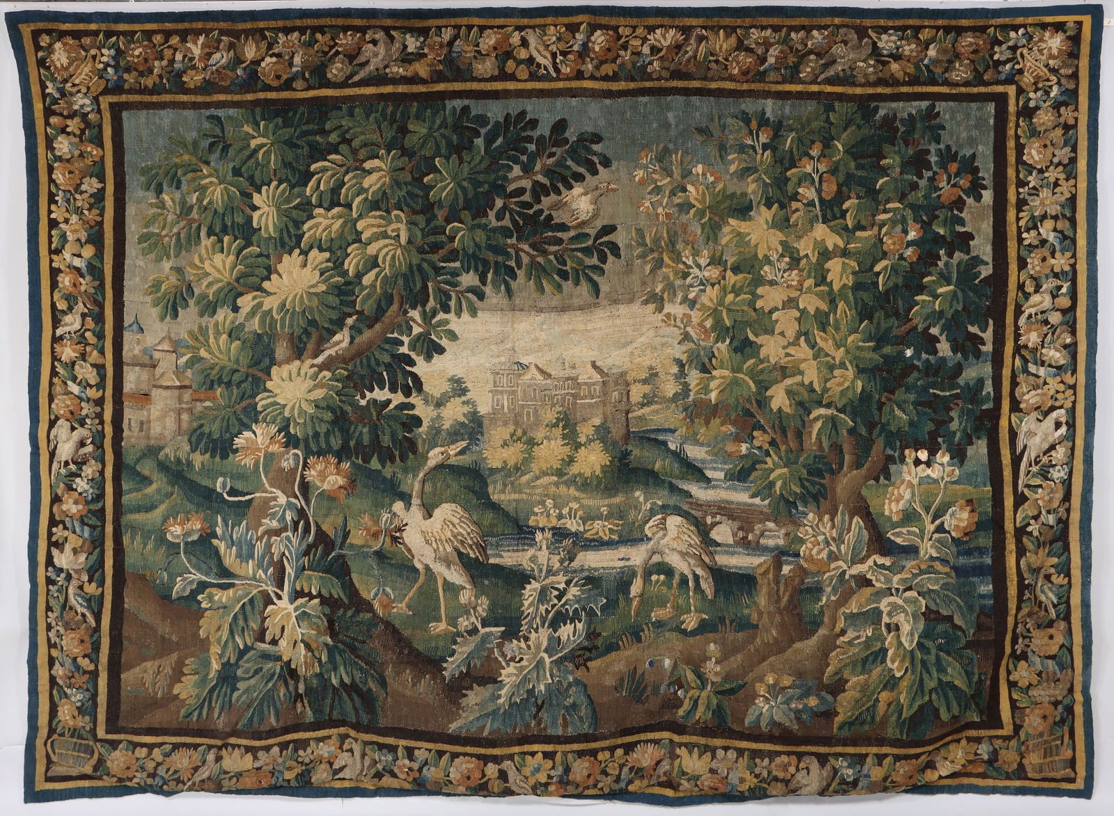 17th Century Flemish Verdure Tapestry: 17th Century Flemish Verdure Tapestrydepicting exotic birds in a lush, verdant landscape with a stream and chateaus in the background, having a border with flowers and birds.106 x 140 in. (269.2 x 355