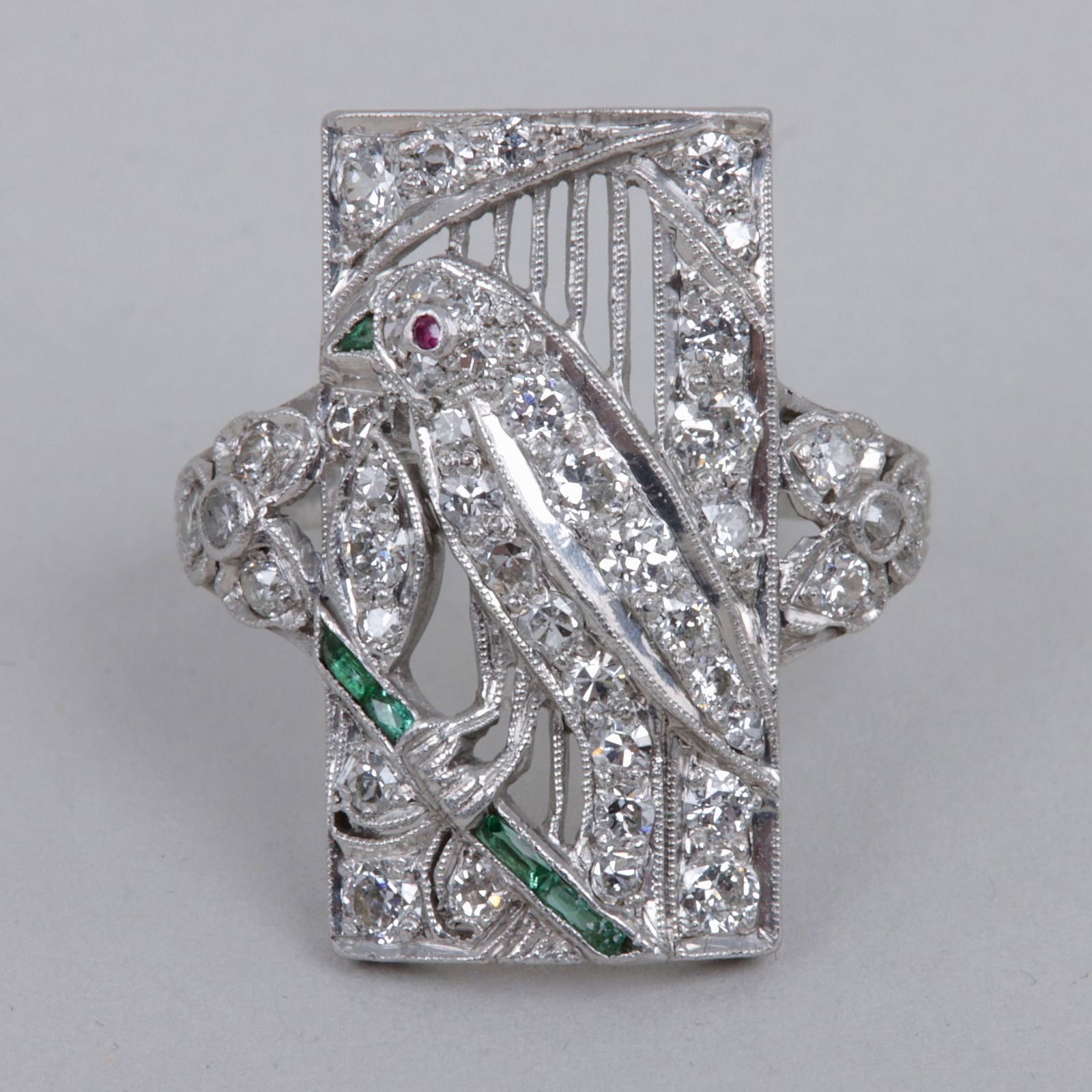 Art Deco Platinum Bird Ring: Art Deco Precious Stones and Platinum Bird Ringhaving a pierced platinum rectangle depicting a bird perched on a branch, the bird having a ruby cabochon eye, triangular-cut emerald beak, and body with