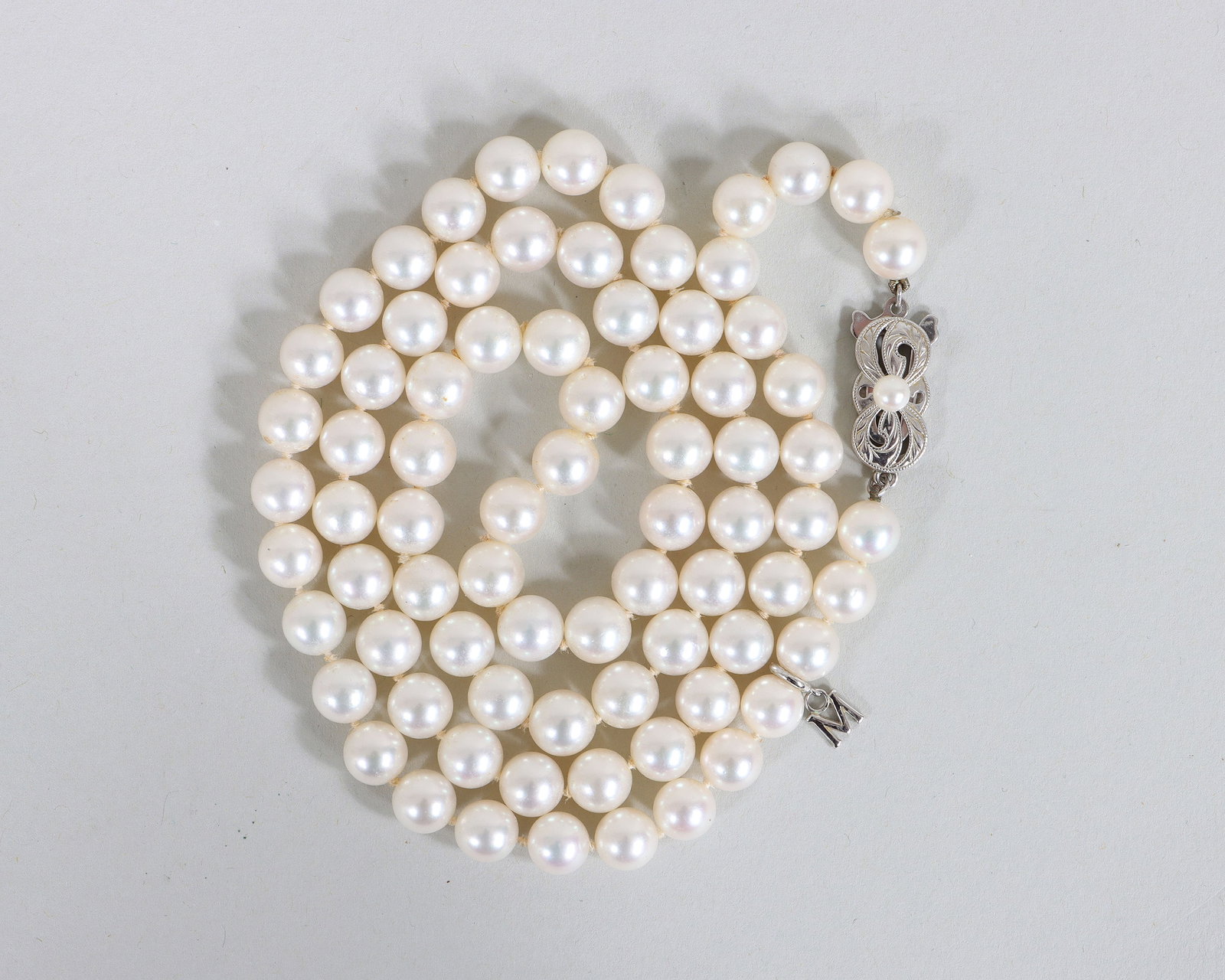 Mikimoto Akoya Pearl Necklace: Mikimoto Akoya Pearl Necklace having a strand of cultured Akoya pearls, all approximately 6.5mm in diameter, with a Mikimoto "M" charm near the clasp, the 18k white gold clasp with scrolled design and