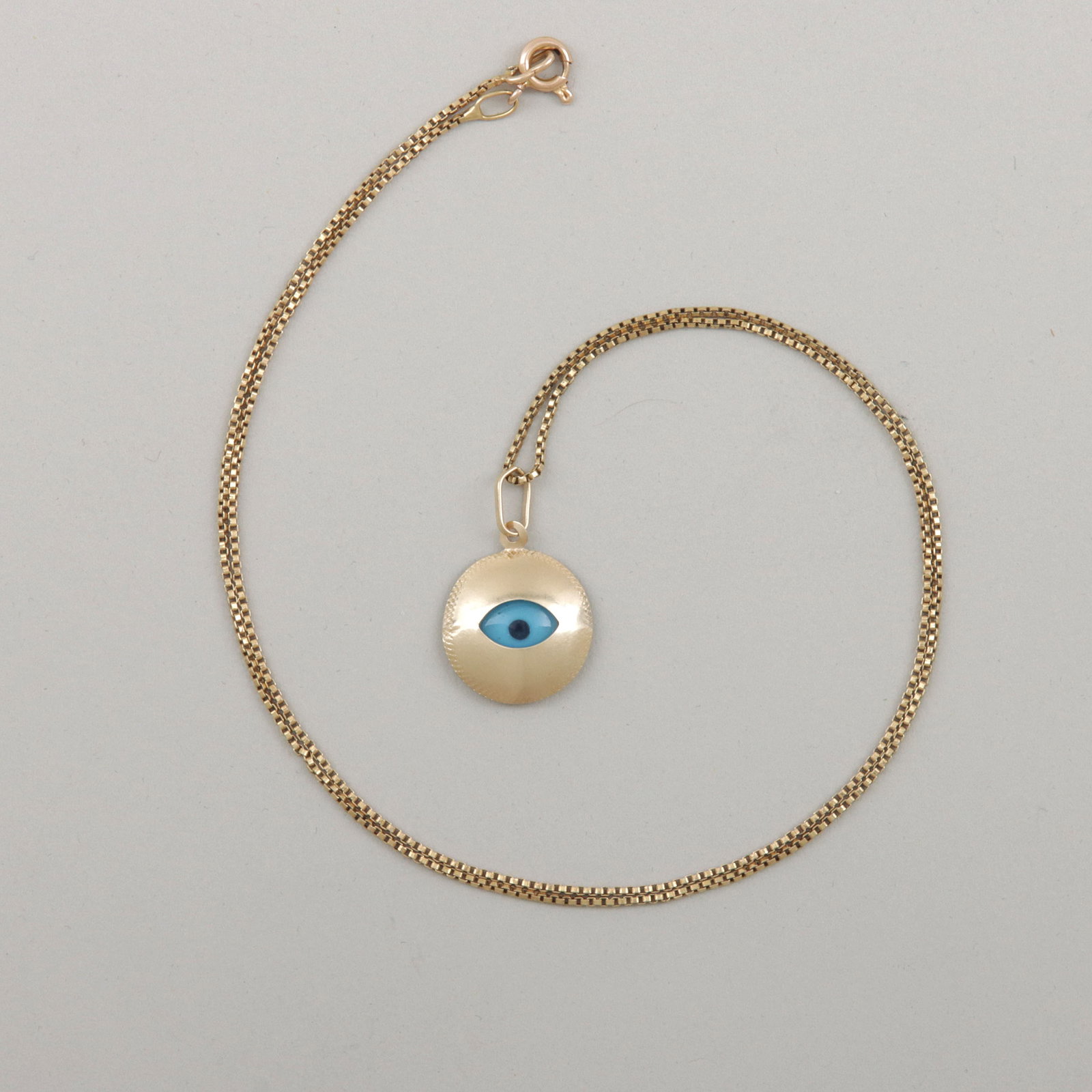 Gold Evil Eye Pendant Necklace: Gold Evil Eye Pendant Necklace having glass "evil eye" in 14k gold frame with textured border, on 18k box chain with 14k gold clasp, marked on bail of pendant and clasp. Length (open) 17 1/4 in. (43.8