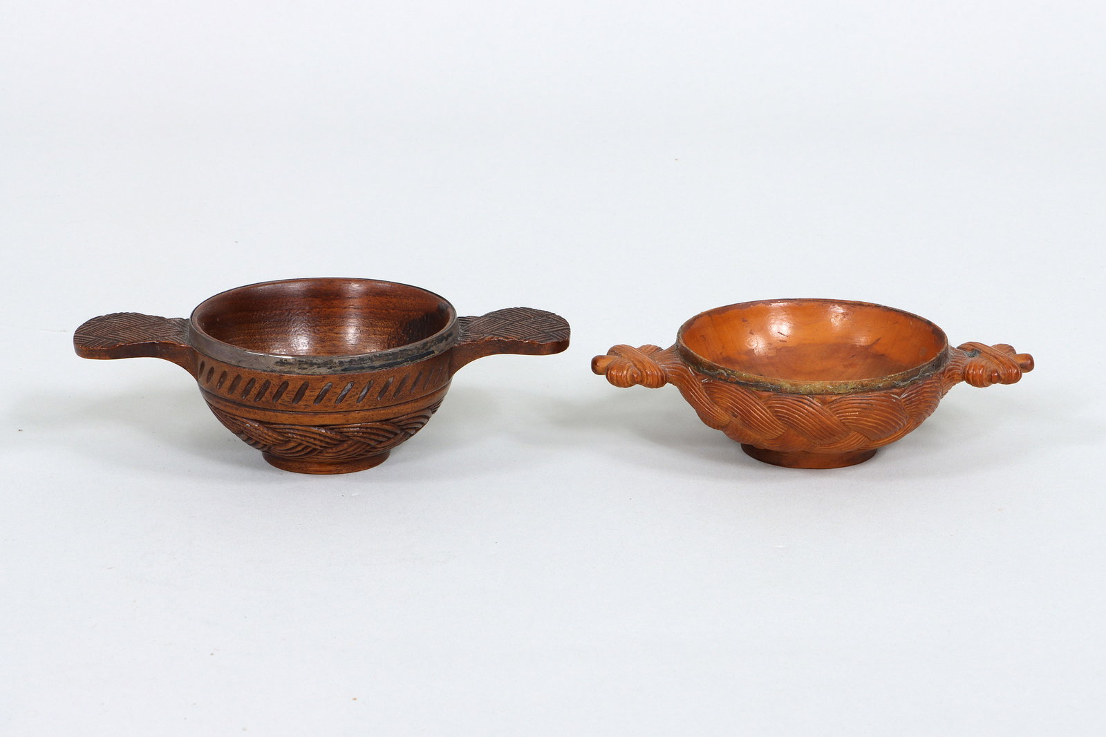 Scottish Carved Wood Quaichs: Group of (2) Scottish Carved Wood Quaichs having twin handles and bodies with plaited design, to include: silver-mounted quaich, having applied silver rim, handles with crosshatching, top border with 
