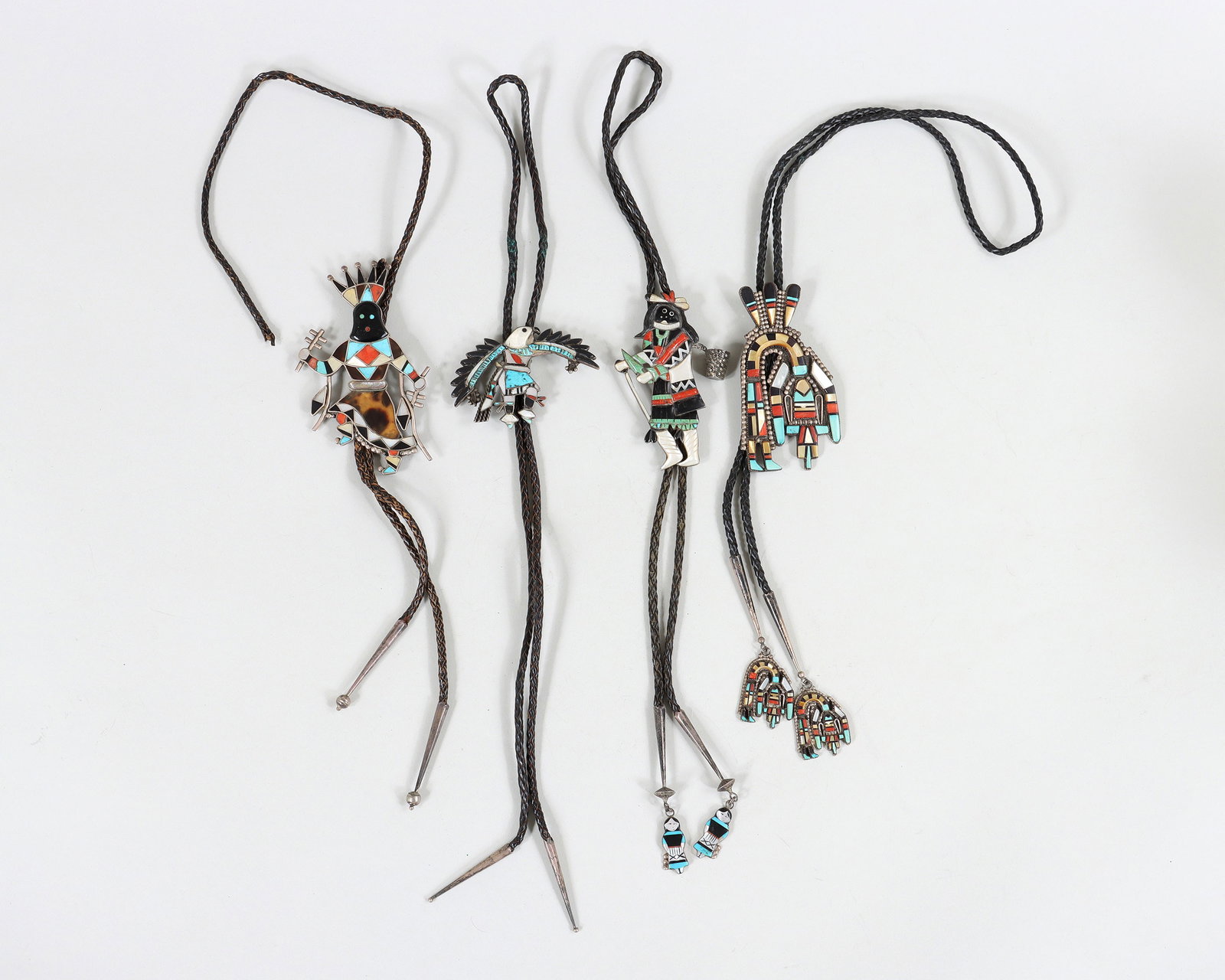 Native American Silver Katsina and Kachina Bolo Ties: Group of (4) Native American Mosaic Inlay Silver Katsina and Kachina Bolo Ties all having silver katsina or kachina figural bolos with inlaid mother-of-pearl, turquoise, coral, onyx or jet, and possib