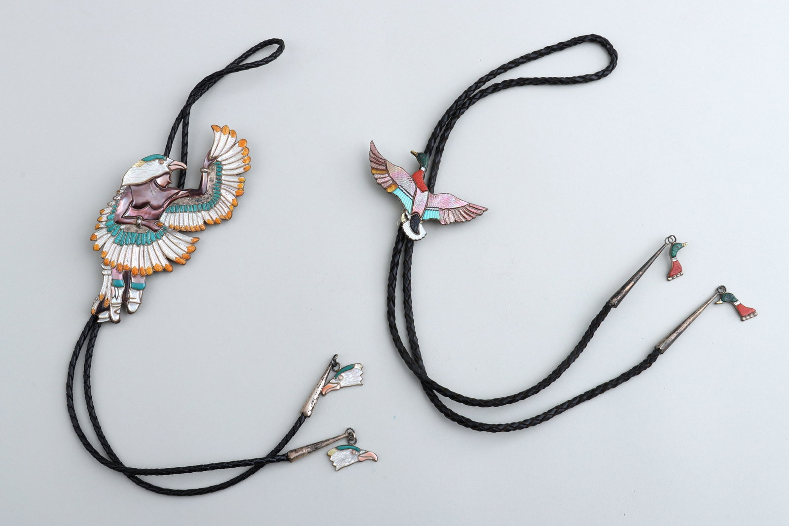 Native American Mosaic Inlay Silver Bolo Ties: Group of (2) Native American Carved Mosaic Inlay Silver Bolo Ties the figural silver bolos having stone and shell inlay with carved decoration, on braided leather cords with silver tips ending in char