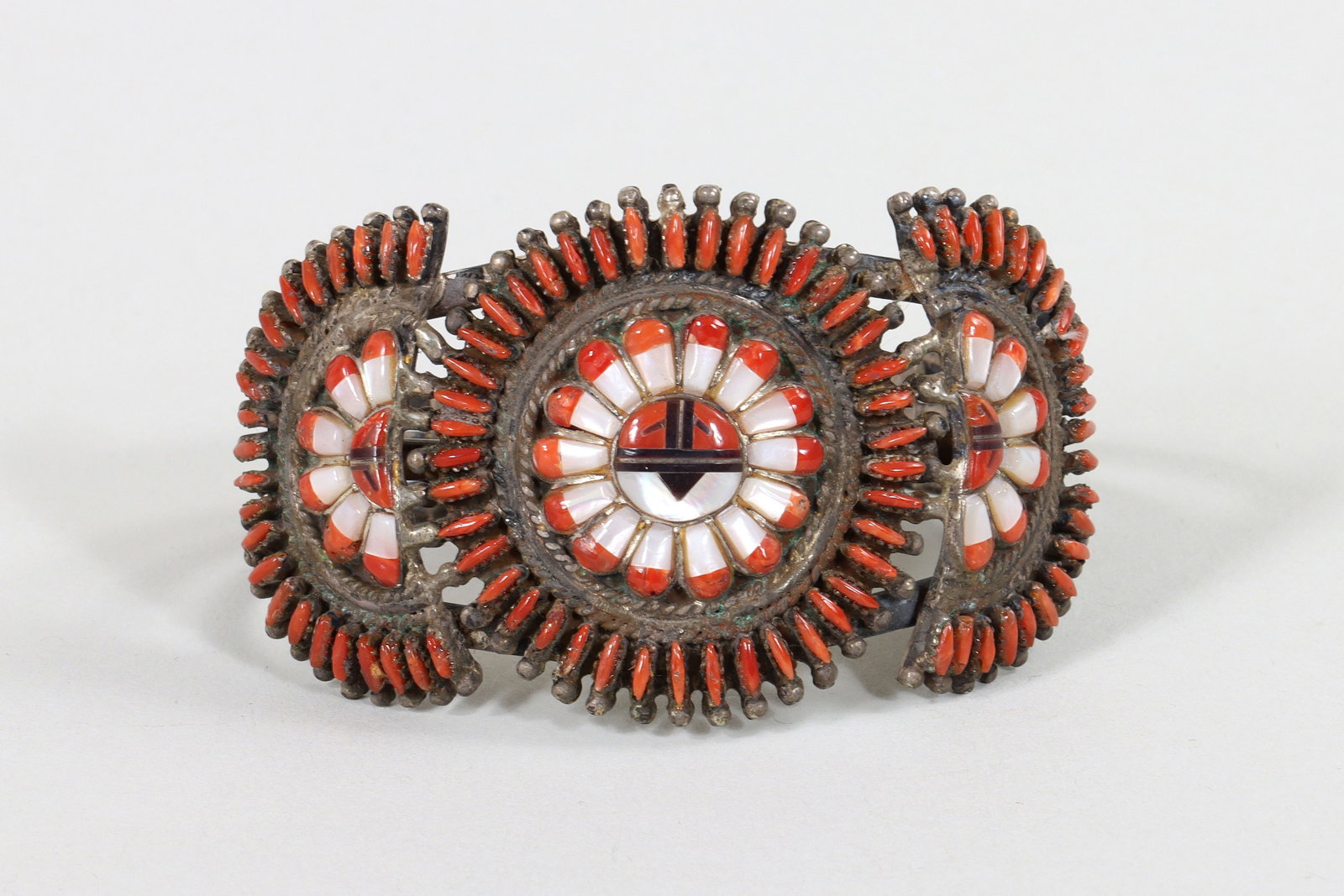 Zuni "Sunface" Sterling Bracelet: Zuni "Sunface" Mosaic Inlay and Needlepoint Sterling Silver Cuff Bracelet having "Sunface" mosaics with inlaid coral, mother-of-pearl, and purple spiny oyster, all surrounded by needlepoint coral bord