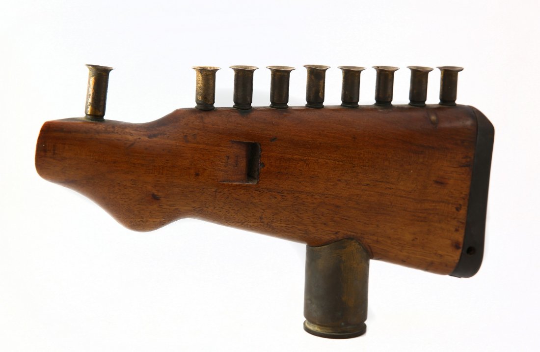 A Chanukah menorah made from a rifle butt and shells.: An original Chanukah menorah made from a wooden rifle butt. Israel, 1960s. The body of the menorah is made of wood, and on it are 9 candle holders made of the rifle's shells. The menorah's stand is al