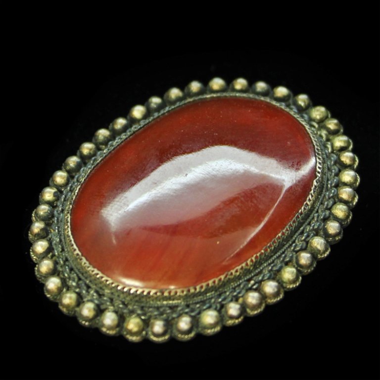 Chinese Carnelian Brooch in Silver: Est. $ 200-300 Chinese Carnelian Brooch in Silver 15.21 grams total weight. Chinese marked brooch. Oval design incorporation bead, chain and mesh texture. 1 3/4" x 1 3/8". Center stone Oval polis smoo