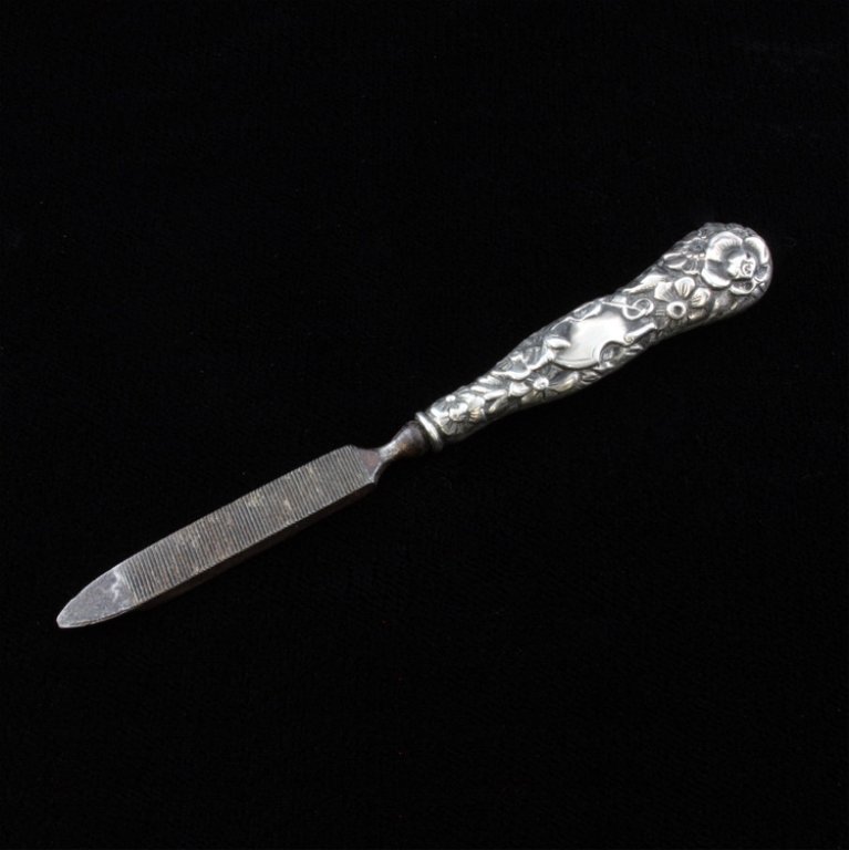 Simons Brothers Sterling Nail File: Est $ 20-45 Sterling marked nail file decorated with a relief floral pattern that bears the Simons Brothers makers mark. 3 3/4" long x 1/2" wide and weighs .34 ozt.