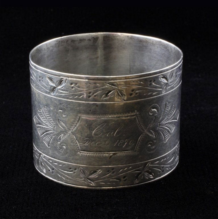 Silver Napkin Ring: Est $ 20-45 Silver napkin ring marked 52 with a floral and etched design. Engraved on the ring says "Cal Dec 0 1870." The ring measures 1 1/4" tall x 1 3/4" in diameter and weighs .6 ozt.
