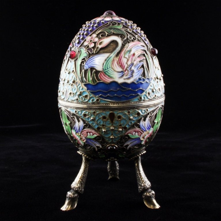 Silver Russian Cloisonné Egg: Est $ 1000-1500 Silver and gilt cloisonné enamel decorative egg depicting swans in water with a gilt interior standing on a tripod of goat's feet. The marks inside the egg include the Moscow Kokoshni