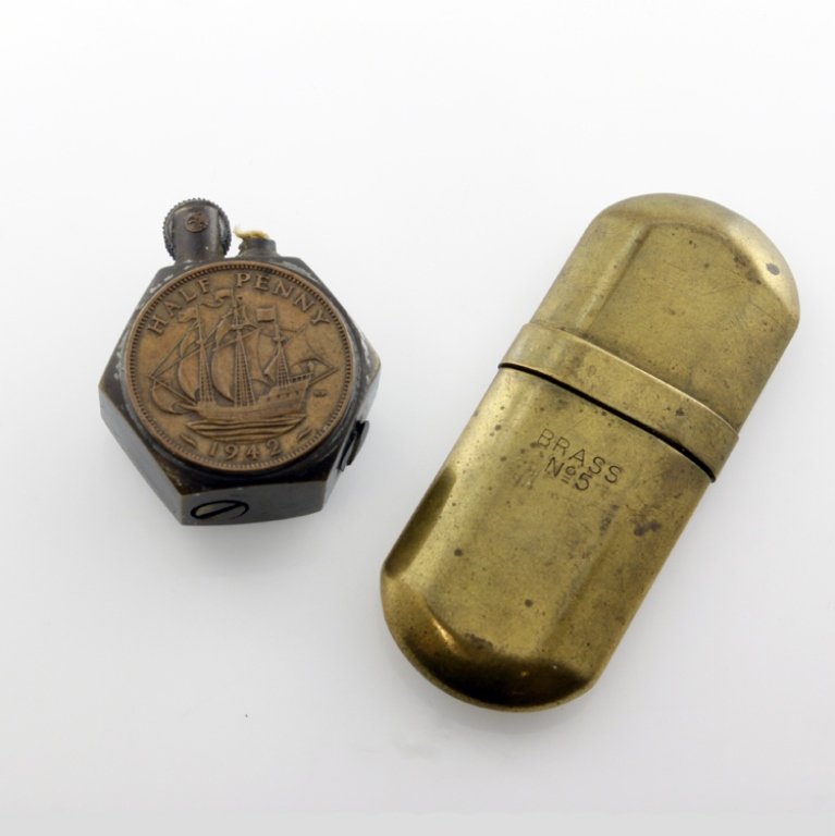 Set of Two Vintage Lighters: Est. $10 - 20 Set of Two Vintage Lighters. (1) Small brass capsule shaped lighter. Minor wear. Measures 2.5" long. (1) small hexagonal lighter with coin appliques on either side.