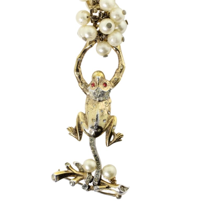 Trifari With Crown Hanging Monkey Brooch: Est. $ 80 - 120 Trifari With Crown Hanging Monkey Brooch. Brooch with a monkey hanging by tail holding faux pearly fruit. Gold tone with rhinestones, gemstones, and faux pearl accents. Mark: Trifari w