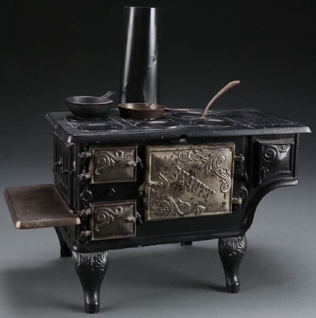 A CHILD'S CAST IRON TOY “BEAUTY” COOK STOVE: A CHILD'S CAST IRON TOY “BEAUTY” COOK STOVE, EARLY 20TH CENTURY. With embossed name on oven door. Length 13.25 inches (33.6 cm). SHIPPING NOTICE:Jackson’s is your sole and only source for one s
