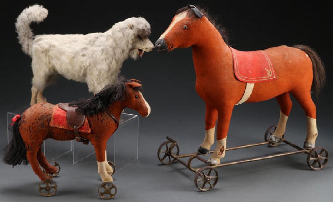 THREE VINTAGE ANIMAL PULL TOYS, EARLY 20TH C: THREE VINTAGE ANIMAL PULL TOYS, EARLY 20TH CENTURY. Comprising a large felt horse on iron carriage, a felt horse with leather saddle, and a white fur dog. The largest length 16.5 inches. SHIPPING NOTI
