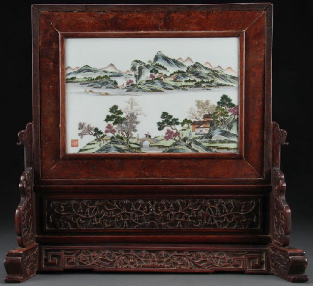 CHINESE FAMILLE ROSE PORCELAIN SCHOLARS SCREEN: A CHINESE FAMILLE ROSE SCENIC PORCELAIN AND CARVED HARDWOOD SCHOLARS SCREEN. Of rectangular form depicting a tree lined harbor with figures and pavilions and mountainous background and with Qianlong a