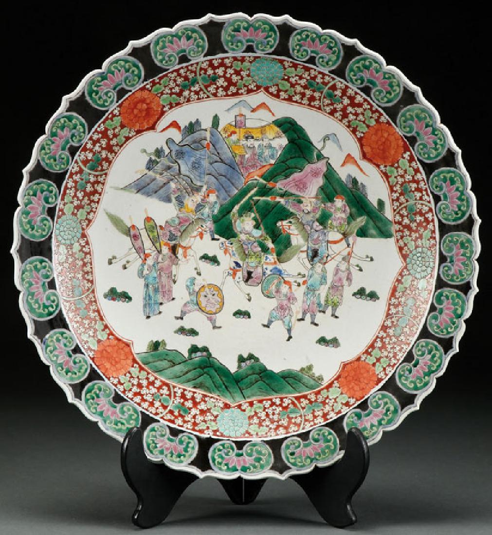 A LARGE CHINESE FAMILLE VERTE PORCELAIN CHARGER: A LARGE CHINESE FAMILLE VERTE PORCELAIN CHARGER. Decorated with a scene of warring figures in a mountain setting. Surrounded by a Ruyi head and foliate scalloped rim. The verso with Tongzhi reign mark
