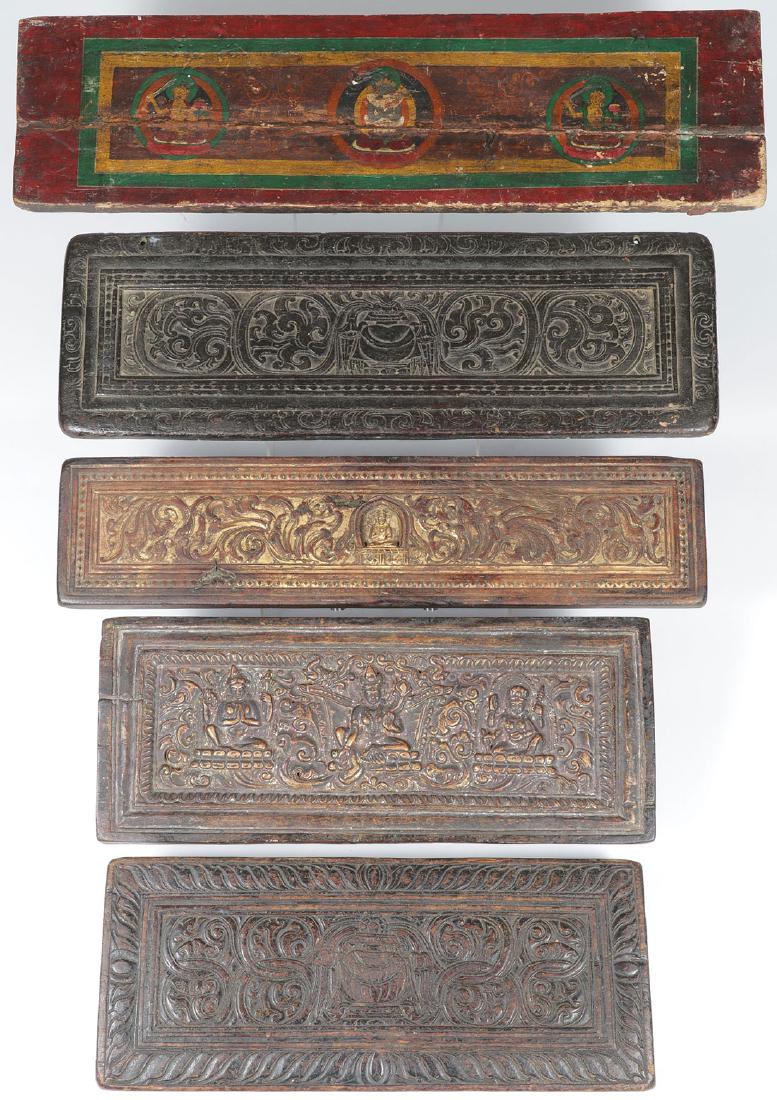 5 TIBETAN CARVED POLYCHROME AND GILT SUTRA COVERS: FIVE TIBETAN CARVED POLYCRHOME AND GILT SUTRA COVERS, 18TH/19TH CENTURY. The largest painted with three seated Buddhist deities, one carved in high relief also with three Buddhist deities resting on d