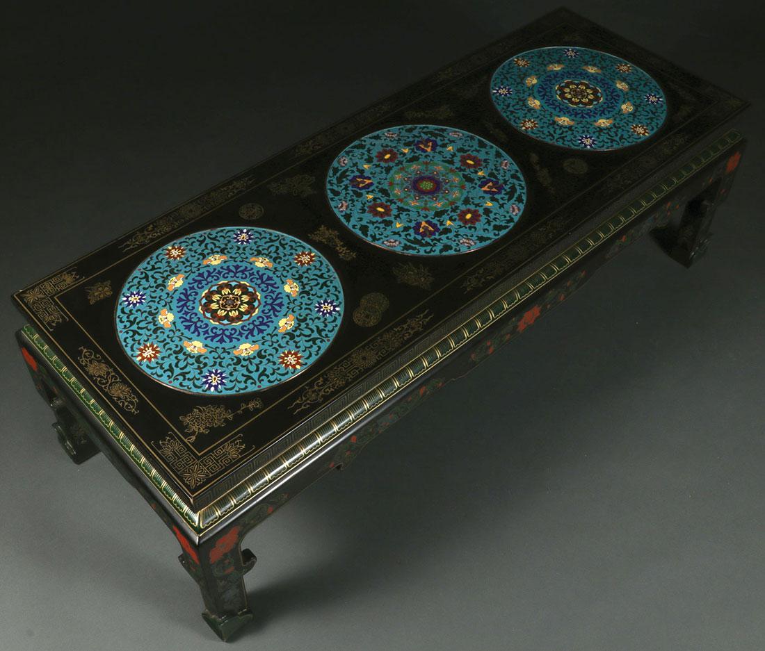 A CHINESE LACQUER WEAR AND CLOISONNÉ TABLE: A CHINESE LACQUER WEAR AND CLOISONNÉ DECORATED TABLE. The rectangular table in black lacquer painted with scrolling foliage and florals and the top set with three large cloisonné medallion discs. Le