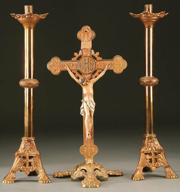 ALTAR CRUCIFIX AND CANDLE STANDS. A unique and o: ALTAR CRUCIFIX AND CANDLE STANDS. A unique and ornate gilt bronze cross resting on an open work three-footed base upon which is mounted a poly-chrome cast metal corpus. Height 20 inches. Together with