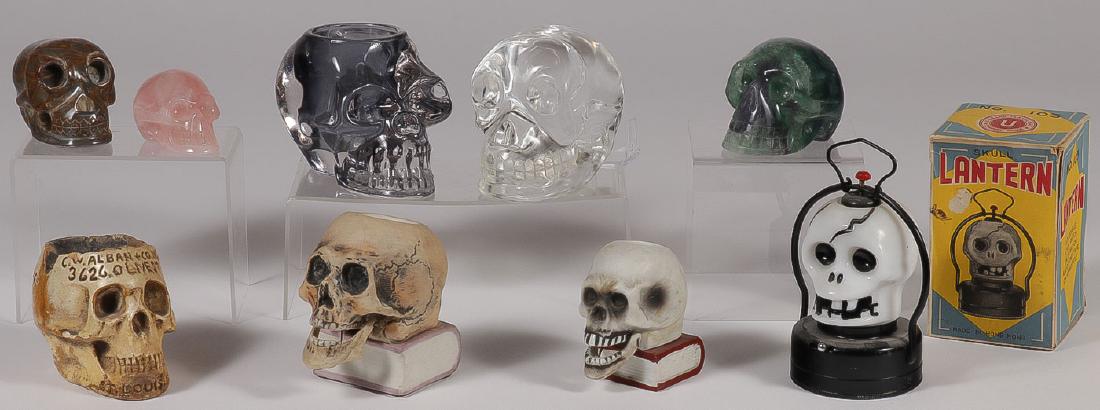 NINE NOVELTY SKULLS: NINE NOVELTY SKULLS. Comprising a novelty battery operated skull lantern with milk glass shade and original box, two bisque skulls resting on book toothpicks with articulated jaw, a plaster advertisin