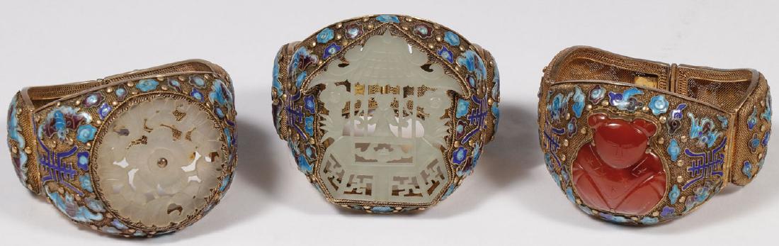 THREE CHINESE SILVER GILT AND ENAMELED FILLIGREE: THREE CHINESE SILVER GILT AND ENAMELED FILLIGREE BRACELETS. Two mounted with pierced carved jade pendants, the other set with a relief carved carnelian seated figure. Each bracelet in gilded silver fi