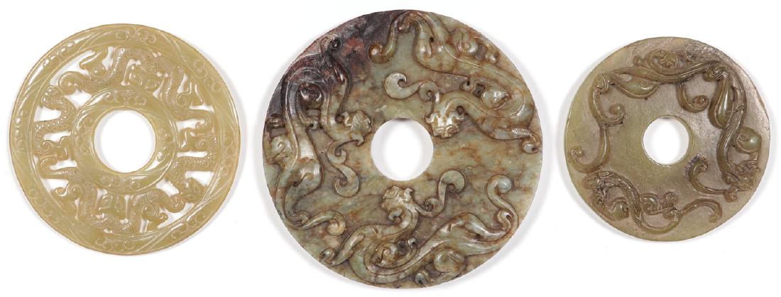 THREE CHINESE CARVED JADE DISCS: THREE CHINESE CARVED JADE DISCS. Comprising a delicate, finely carved, pierced jade disc with central section, bordered with scaled creatures, thin and translucent. Together with a larger solid disc w