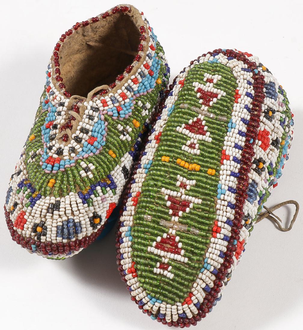 FULLY BEADED PLAINS MOCCASINS, C. 1900: FULLY BEADED PLAINS MOCCASINS, C. 1900. The soft, Native-tanned hide, infant sized shoe forms, fully beaded with geometric designs and colorful banding with a good variety of beads, in excellent c