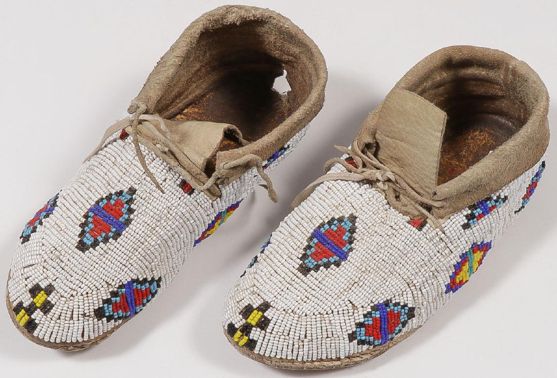 A PAIR OF BEADED PLAINS MOCCASINS, 20TH C: A PAIR OF BEADED PLAINS MOCCASINS, 20TH C. Sinew-sewn with hard soles and beaded geometric designs on a white beaded field. Length 8.5 inches. SHIPPING NOTICE: Jackson's is your sole