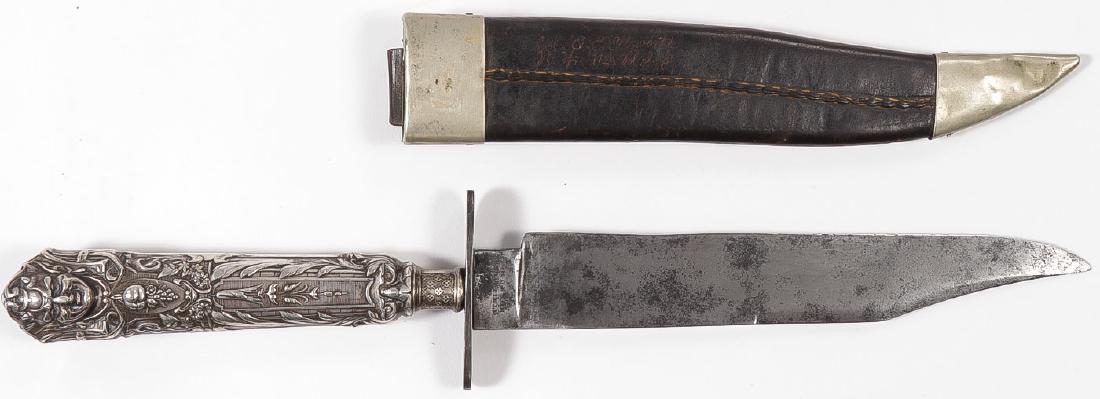 LARGE BOWIE KNIFE & SHEATH BY MANSON: LARGE BOWIE KNIFE & SHEATH BY MANSON. 7-inch clipped-point blade marked on ricasso “MANSON/SHEFFIELD”. Oval guard beneath ornate German silver cast hilt with bachanal motifs, together with