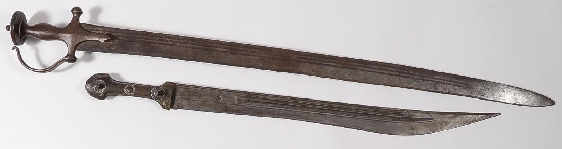 A PAIR OF MUGHAL SWORDS: A PAIR OF MUGHAL SWORDS. Comprising a Tulwar-Tegha style sword with single edged triple fuller blade set in an iron handle with disc pommel and guard, length 37.75 inches (95.9 cm). Together with 