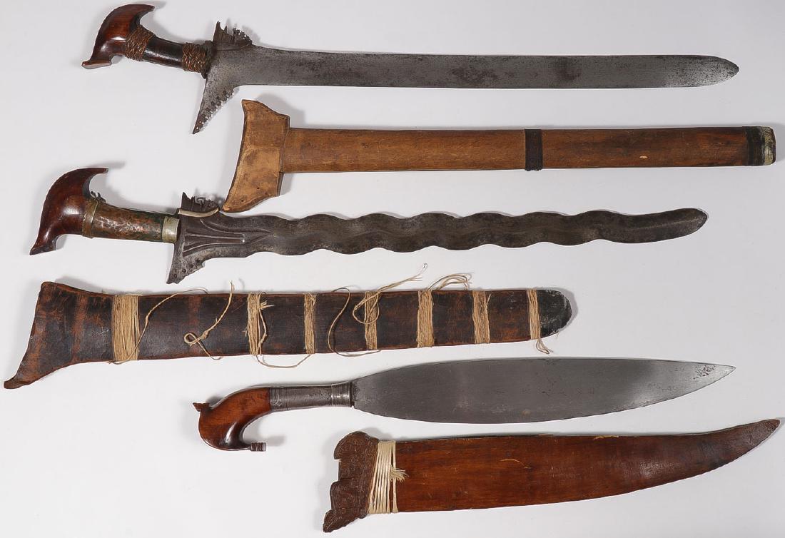 THREE INDONESIAN EDGED WEAPONS: THREE INDONESIAN EDGED WEAPONS. Comprising a pair of kris, each with sheath, together with a smaller spatula blade knife with wooden sheath and carved figural wood pommel, and a carved and polychrome 