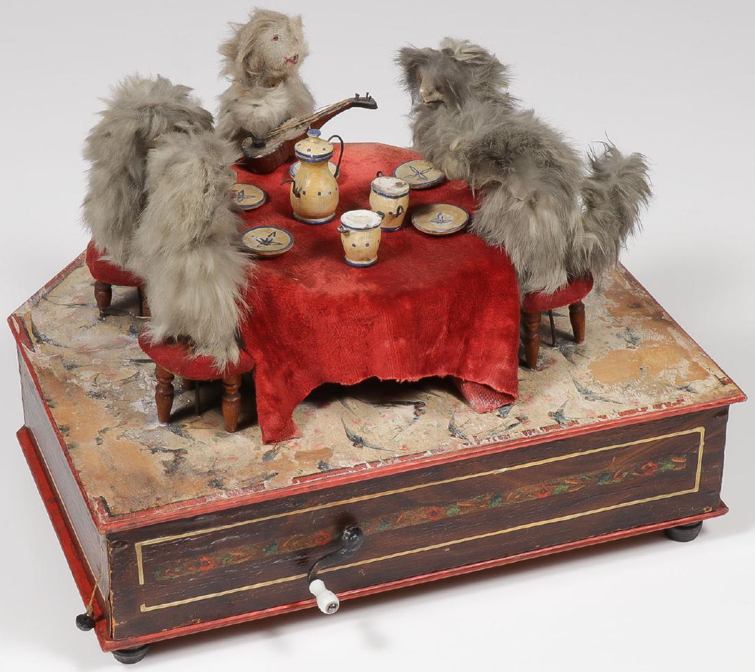 A MANIVELLE AUTOMATON OF CAT'S TEA PARTY, C 1890: A MANIVELLE AUTOMATON OF CAT'S TEA PARTY, C 1890. Comprising a shaped lithographed paper over wood base set with five cats seated at a table set for tea and with hand crank music box and articulat