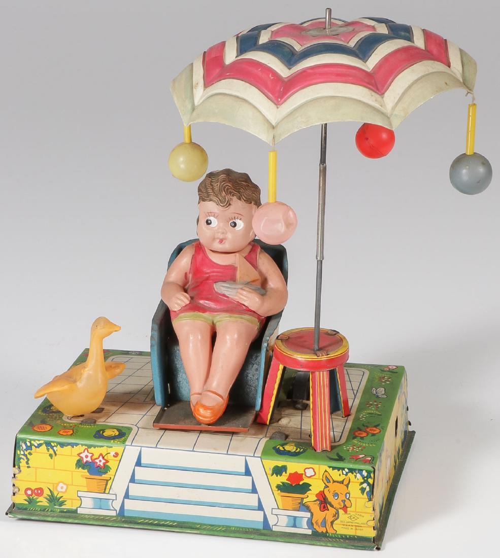 AN ALPS TIN & CELLULOID WIND-UP HAPPY LIFE: AN ALPS TIN & CELLULOID WIND-UP HAPPY LIFE C. 1940. Comprising a celluloid girl in swimsuit holding a toy boat and resting in chair. The tin lithograph base with celluloid duck and three legged t
