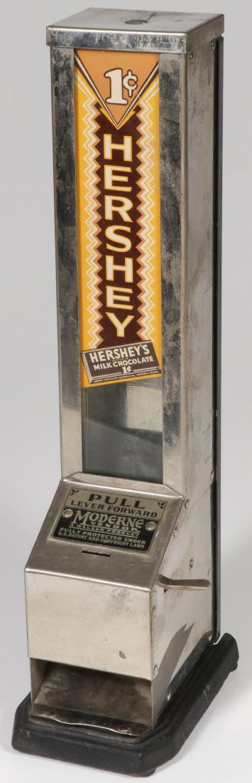 HERSHEY 1-CENT MODERNE VENDOR: HERSHEY 1-CENT MODERNE VENDOR. Chrome on a cast iron base with glass front panel displaying a wonderfully intact "1-cent Hershey" decal. In working condition without key. 17.75 inches 