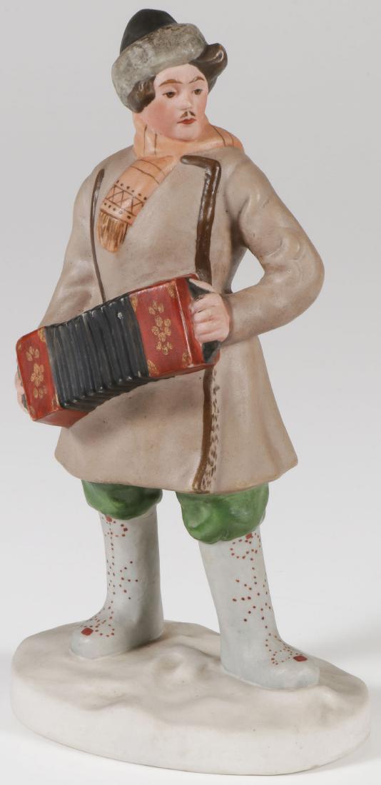 EARLY SOVIET PORCELAIN, DMITRIEVSKY: EARLY SOVIET PORCELAIN FIGURE OF A GARMON PLAYER, DMITRIEVSKY, C.1930. Naturalistically modelled, the young man in winter attire depicted playing a garmon, designed by Boris Kustodiev, underside of ba
