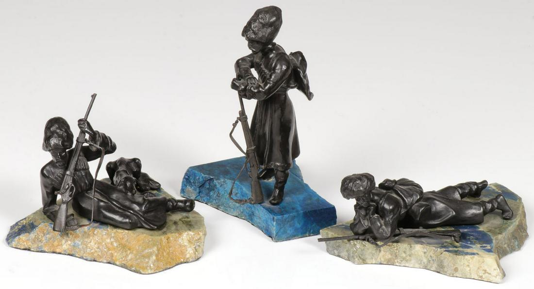 THREE RUSSIAN COSSACK BRONZES: THREE RUSSIAN COSSACK BRONZES. Comprising three patinated bronze figures of Cossack soldiers, two reclining (one with a wolf hound), and the other standing. Each mounted on a polished stone fragment b