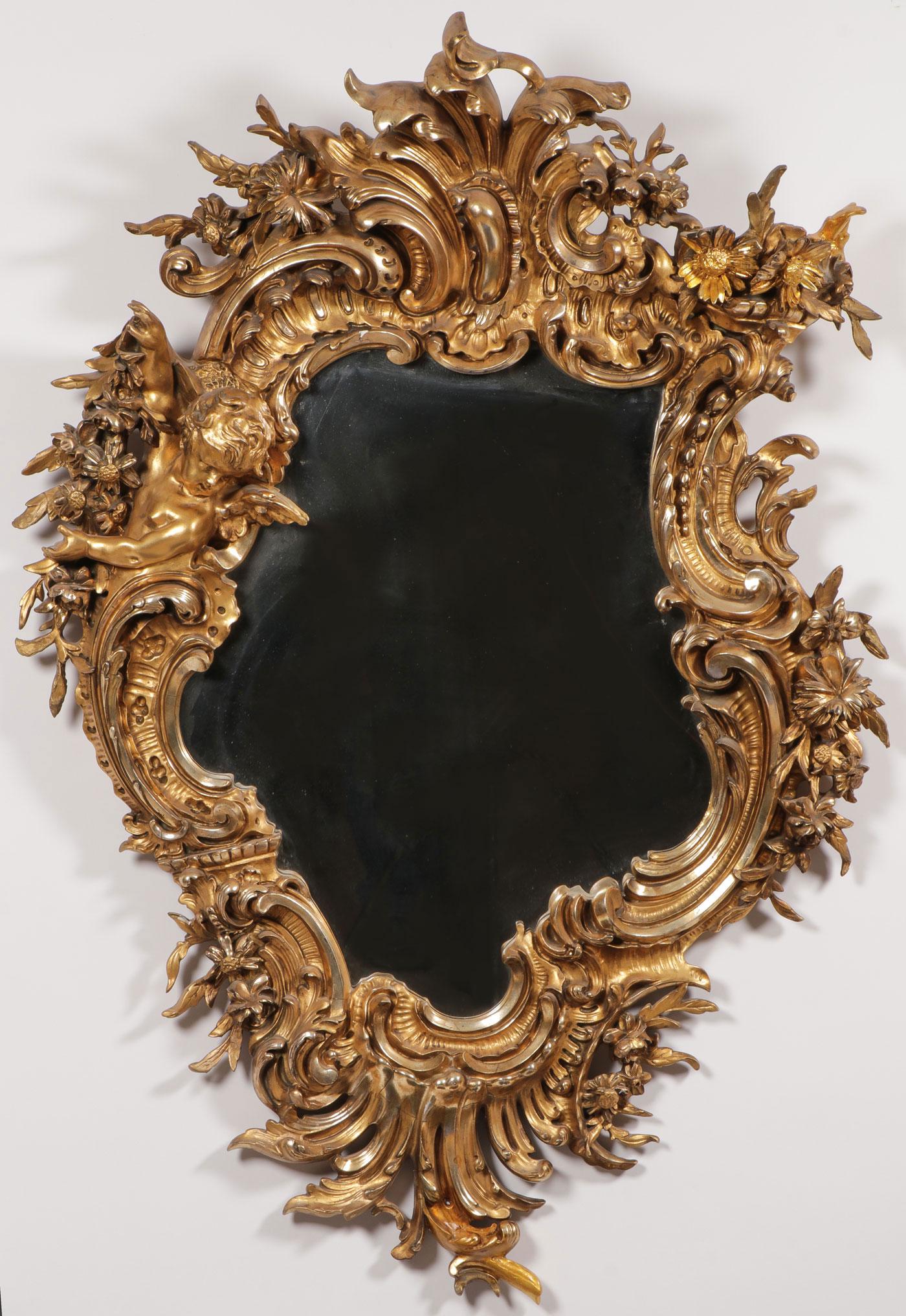 IMPRESSIVE GILT ROCOCO MIRROR, 19TH C: IMPRESSIVE GILT ROCOCO MIRROR, 19TH C. The press molded gilt frame of Rocaille scrolls and applied flower forms, and winged putto framing a shaped mirror. Minor scattered losses and some old repairs. 