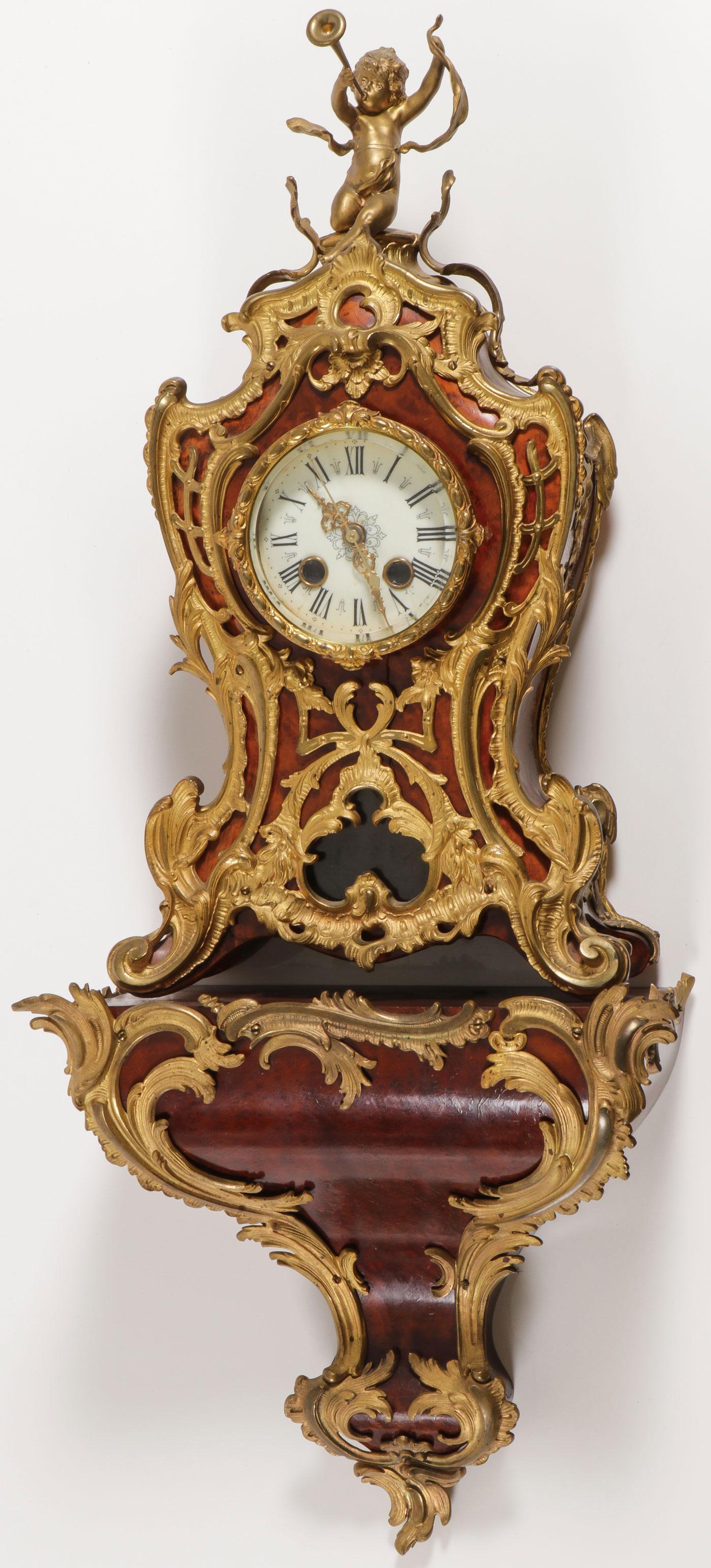 A FRENCH ORMOLU MOUNTED BRACKET CLOCK: A FRENCH ORMOLU MOUNTED BRACKET CLOCK. Comprising an ornate bracket clock on gilt bronze scroll feet, the case overlaid with open work rocaille scrolls and with trumpet blowing putto finial, the inter
