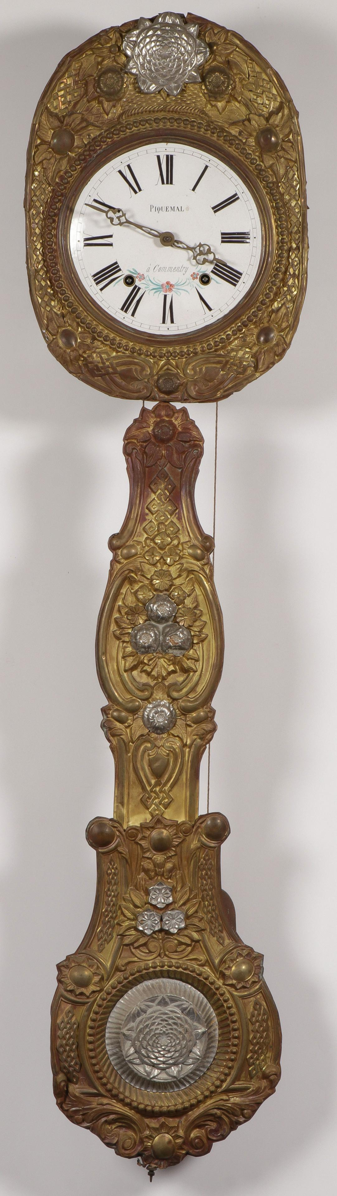 A FRENCH MORBIER CLOCK: A FRENCH MORBIER CLOCK. Comprising an enamel on metal face with Roman numerals, marked "Piquemal a' Commentry" on the dial set in a floral pressed brass surround, suspending a pressed brass decorated 