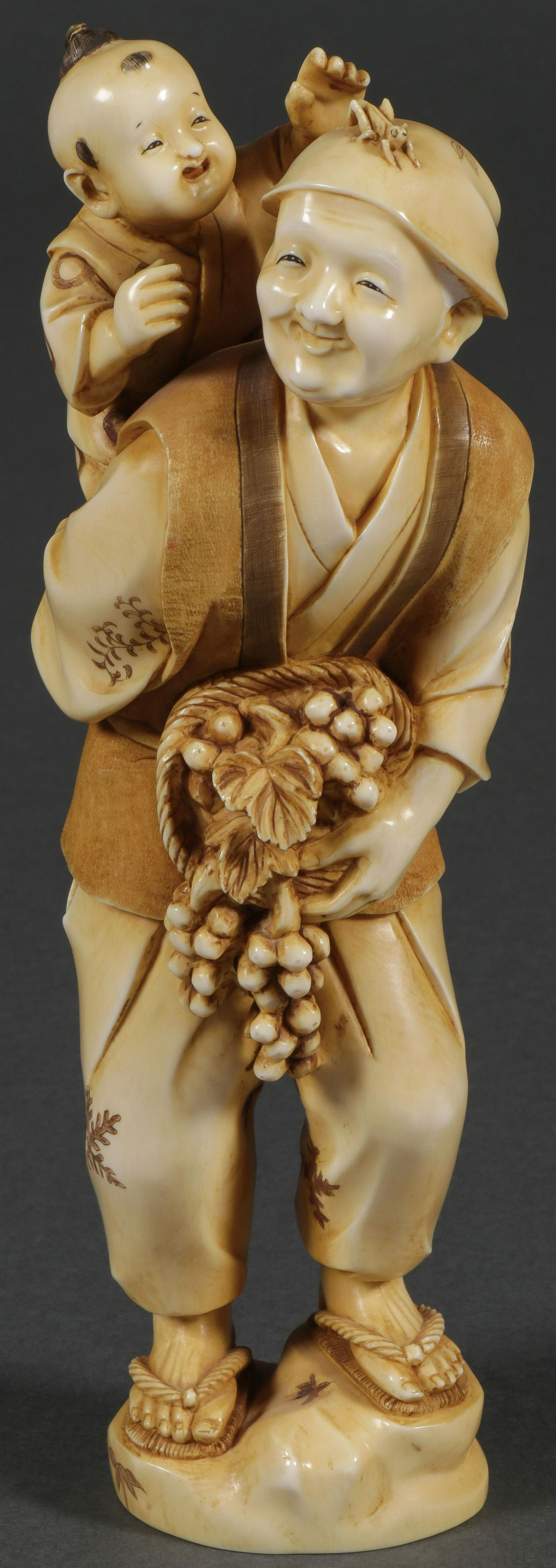 A JAPANESE CARVED OKIMONO, MEIJI: A JAPANESE CARVED OKIMONO, MEIJI. Depicting a grandmother carrying grandchild and holding a basket of grapes. Carved in full round and of good proportions, parts of the surface etched and stained. Und