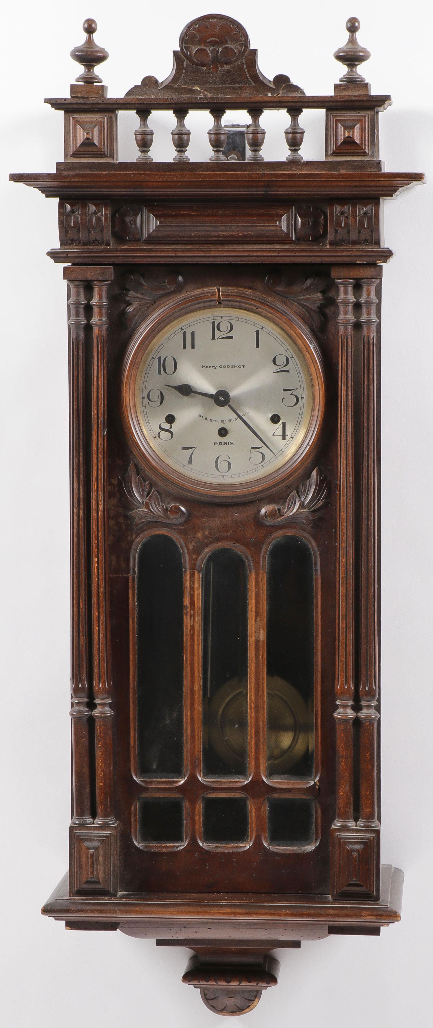 A FINE KIENZLE WALL CLOCK: A FINE KIENZLE WALL CLOCK. Comprising an ornately carved case with intricate balcony formed gallery adorned with finials and arched top above a five panel glazed front flanked by two fluted column for