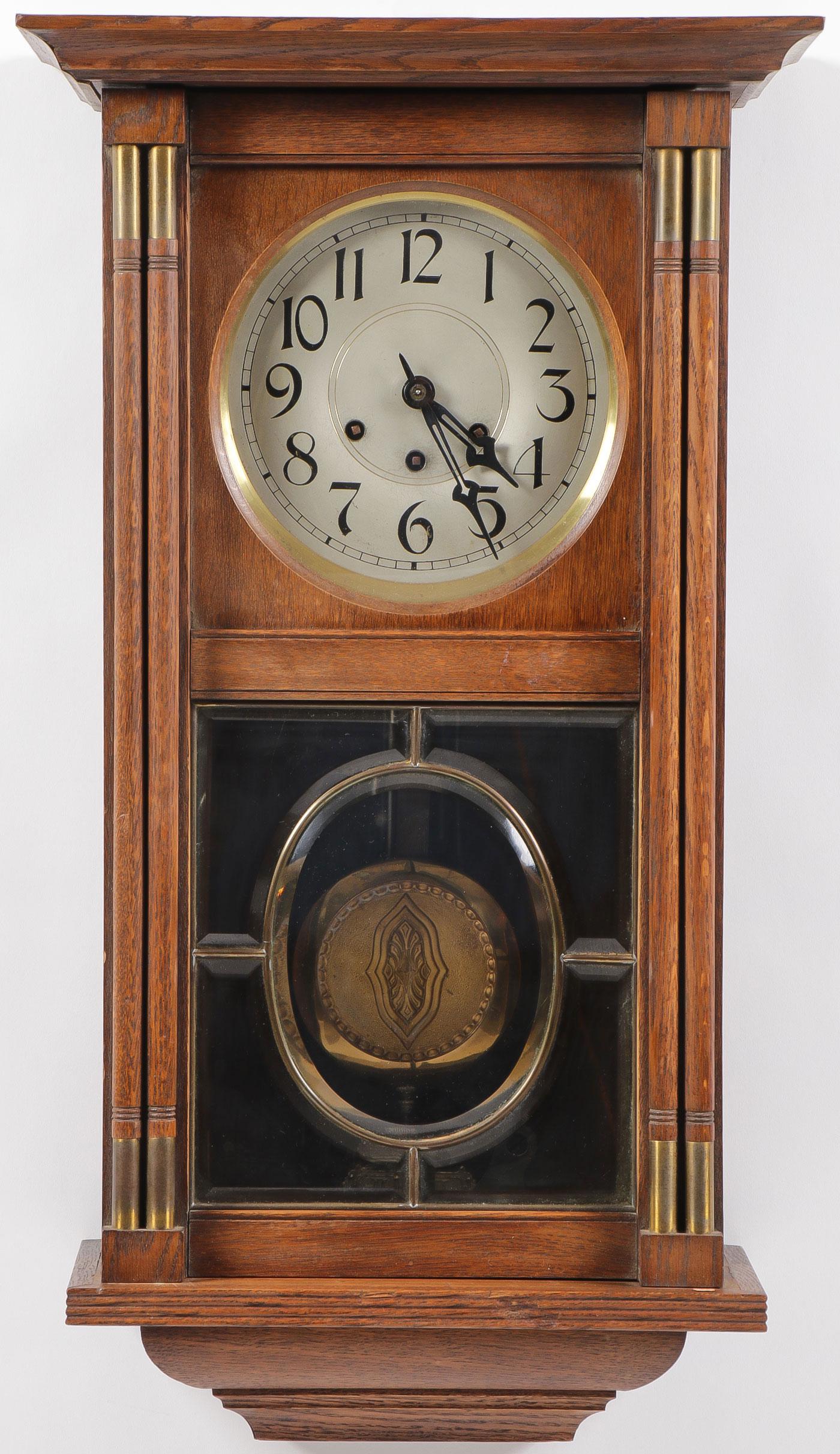 A PAIR OF ART DECO STYLE WALL CLOCKS: A PAIR OF ART DECO STYLE WALL CLOCKS. Comprising an oak case clock with metallic clock face embellished with Arabic numbers above a pendulum all behind a five panel beveled glass door flanked on eith