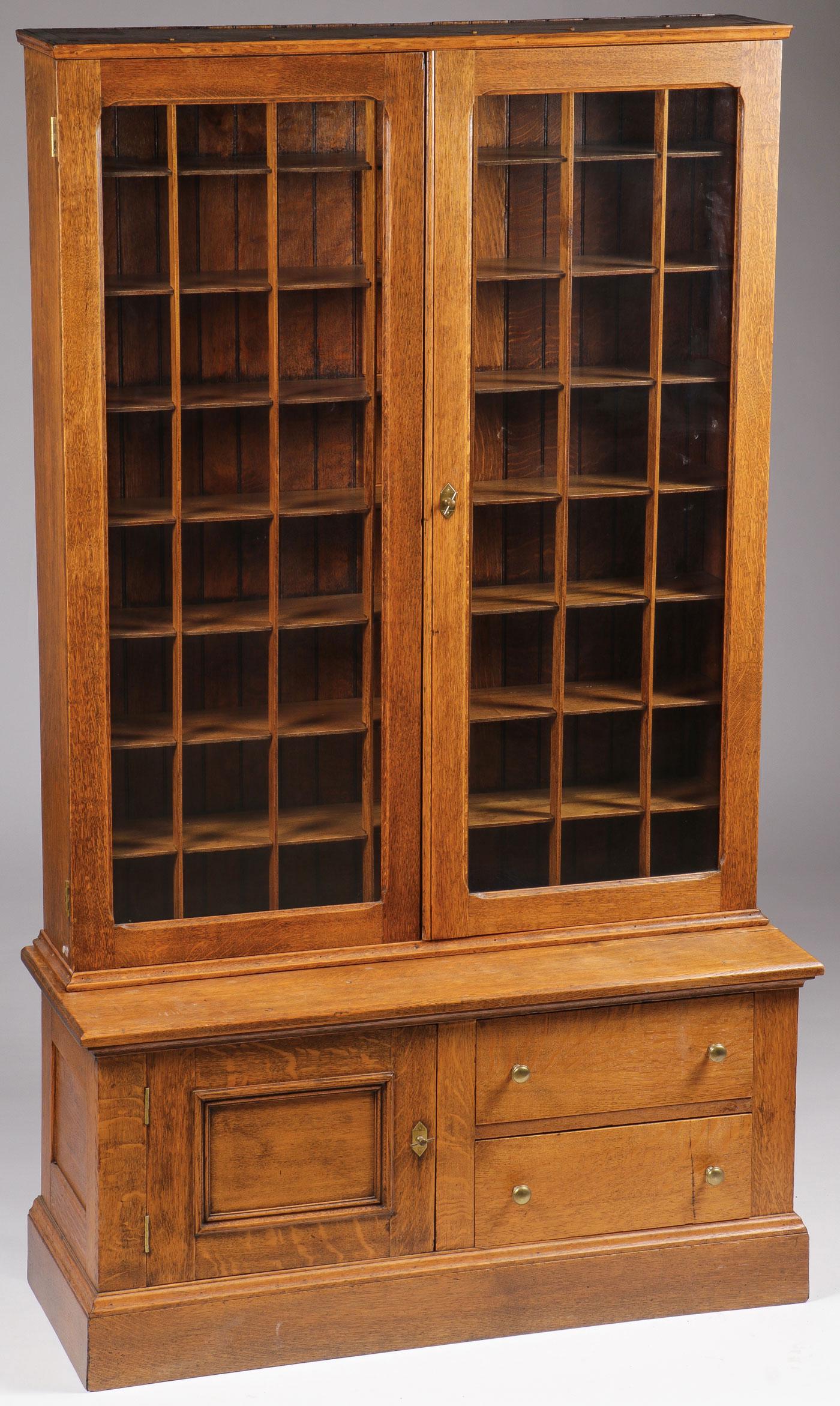 A SPECTACULAR OAK SHAVING MUG CABINET, C. 1890: A SPECTACULAR OAK SHAVING MUG CABINET, C. 1890. Comprising a two-piece cabinet with two large glazed doors opening to reveal eight shelves with 56 separately divided sections, and below a double draw