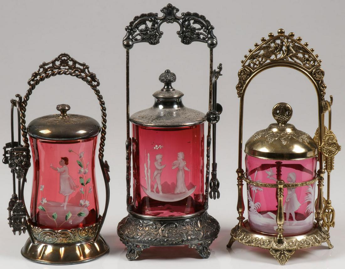 3 MARY GREGORY CRANBERRY PICKLE CASTERS, C. 1890: 3 MARY GREGORY CRANBERRY PICKLE CASTERS, C. 1890. Comprising three individual Bohemian (AKA Mary Gregory) cranberry enamel decorated pickle casters of various shapes and sizes. Each set in an ornate s