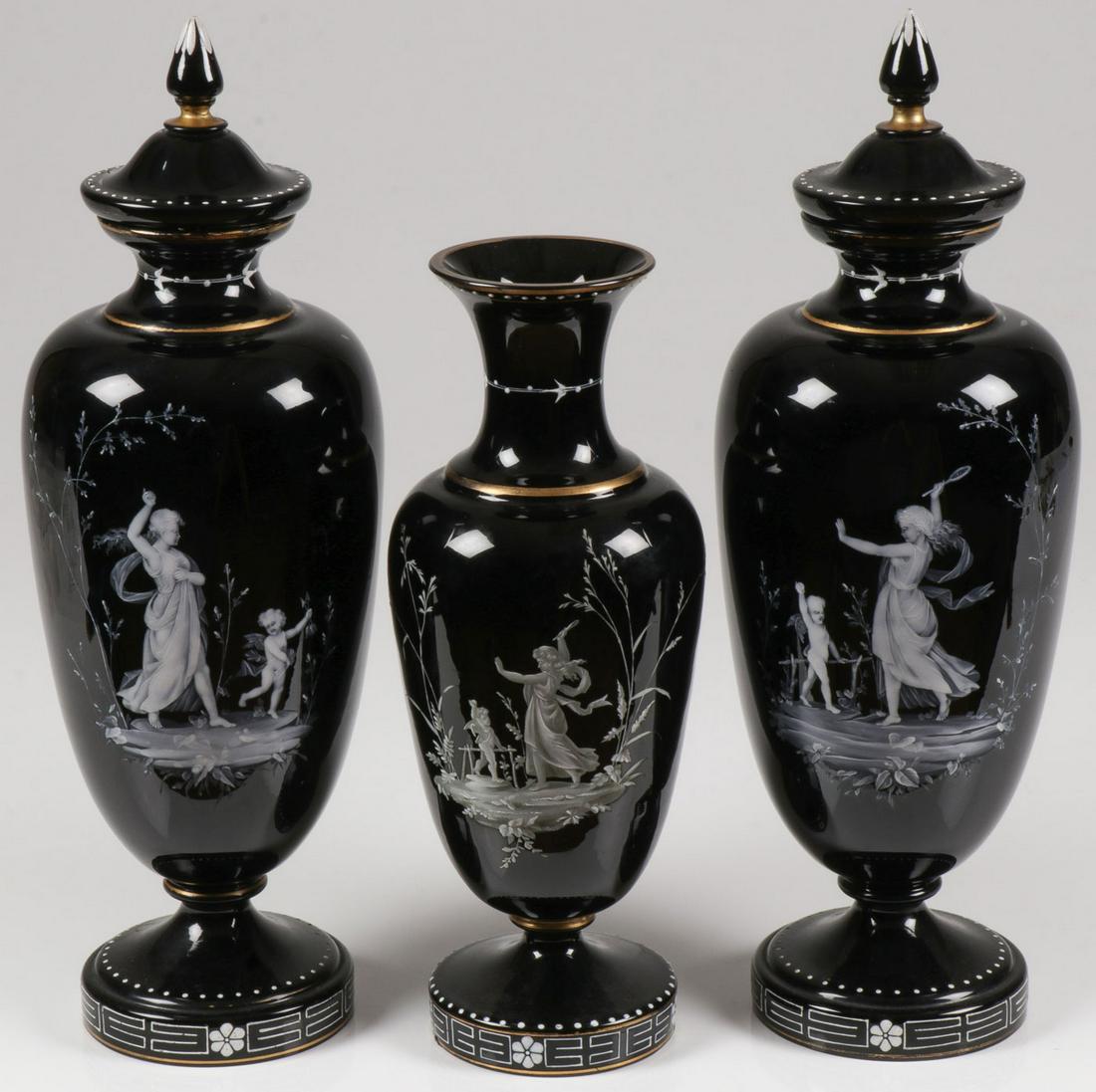 THREE MARY GREGORY MANTLE VASES, C. 1900: THREE MARY GREGORY MANTLE VASES, C. 1900. Comprising a pair of matching black Bohemian (AKA Mary Gregory) enameled art glass lidded urns, each finely painted with women in classical attire being led b