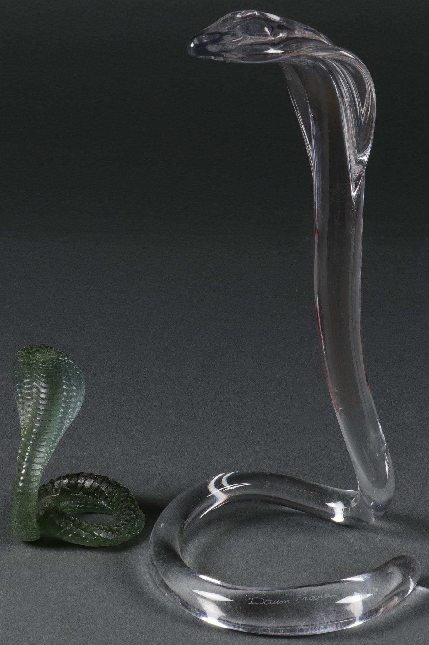 TWO DAUM GLASS COBRAS: TWO DAUM GLASS COBRAS. Comprising two Daum art glass coiled cobras, including one example in clear glass, inscribed on base DAUM, FRANCE, height 14.6 inches (37 cm), as well as smaller example in gree